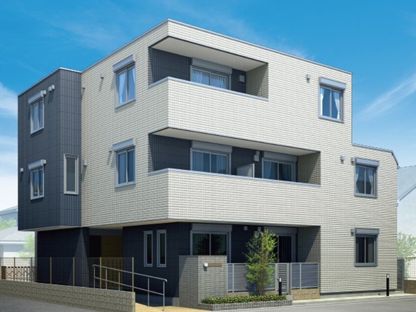 白とグレーの外壁の3階建ての建物は各フロアにベランダがあり、玄関先には手すり付きのスロープもある。