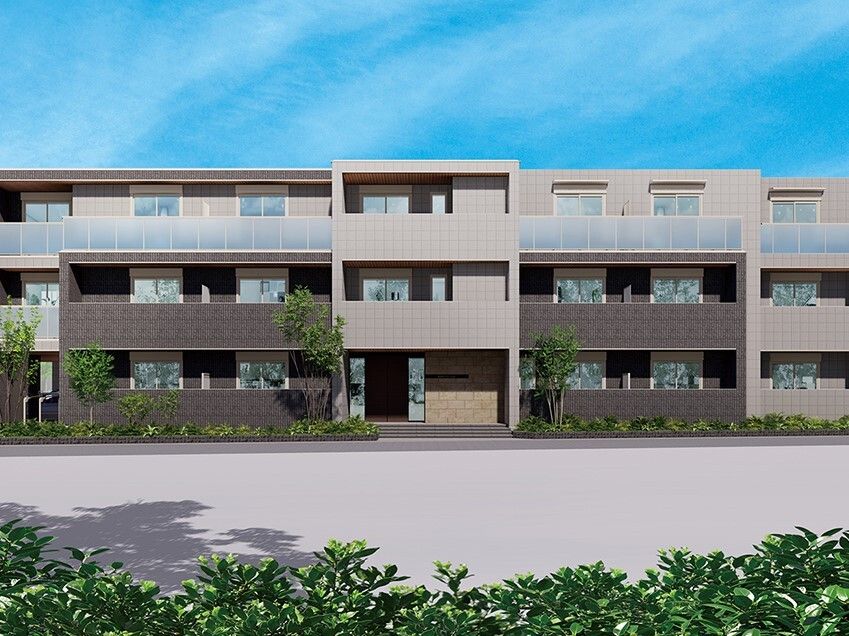 ブラウン系の3階建ての建物の前には広い空き地があり、建物の周りには草木が植えられ、各フロアにベランダがある。