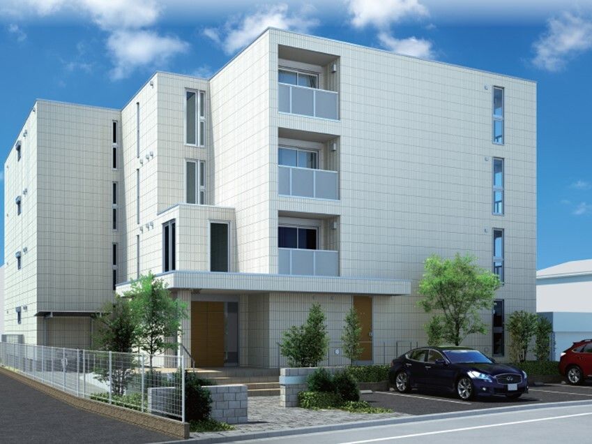 4階建ての建物は日当たりのいい場所に建っている。白を基調としていて、建物のそばの駐車スペースには車も止まっている。