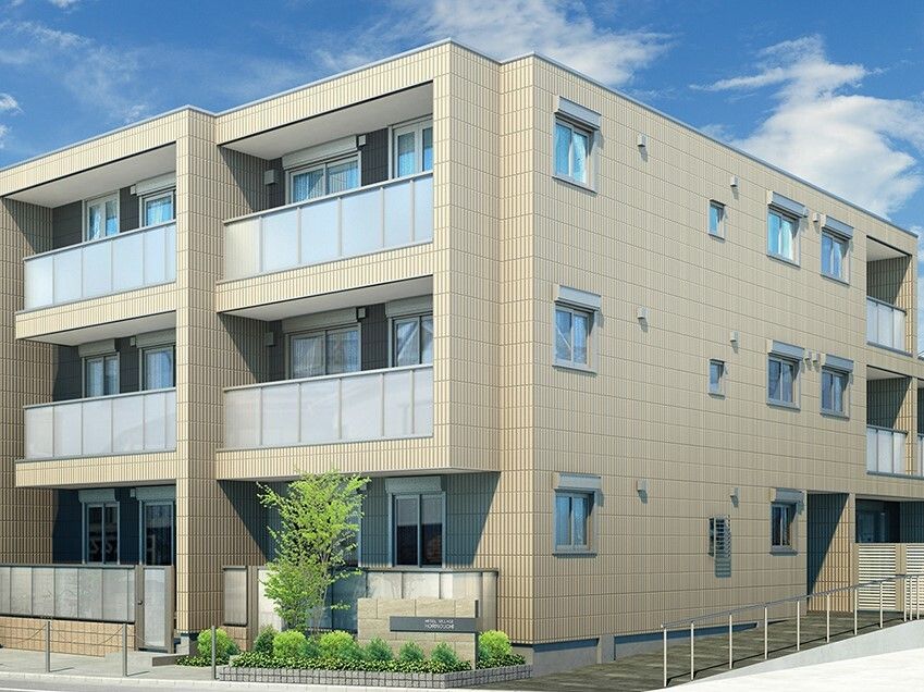 ベージュ系の3階建ての建物の各フロアにベランダがあり、周りには草木が植えられている。
