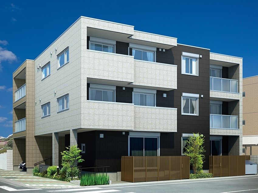 白と黒の3階建ての建物の周りには草木が植えられ、ブラウンのフェンスが付き、一部1階が駐車場となっている。