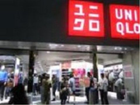衣料量販店の外観である。赤いブランドロゴが開口部上部の外壁にかけられている。開口部は柱のみで、扉はなく、人が自由に出入りしている。