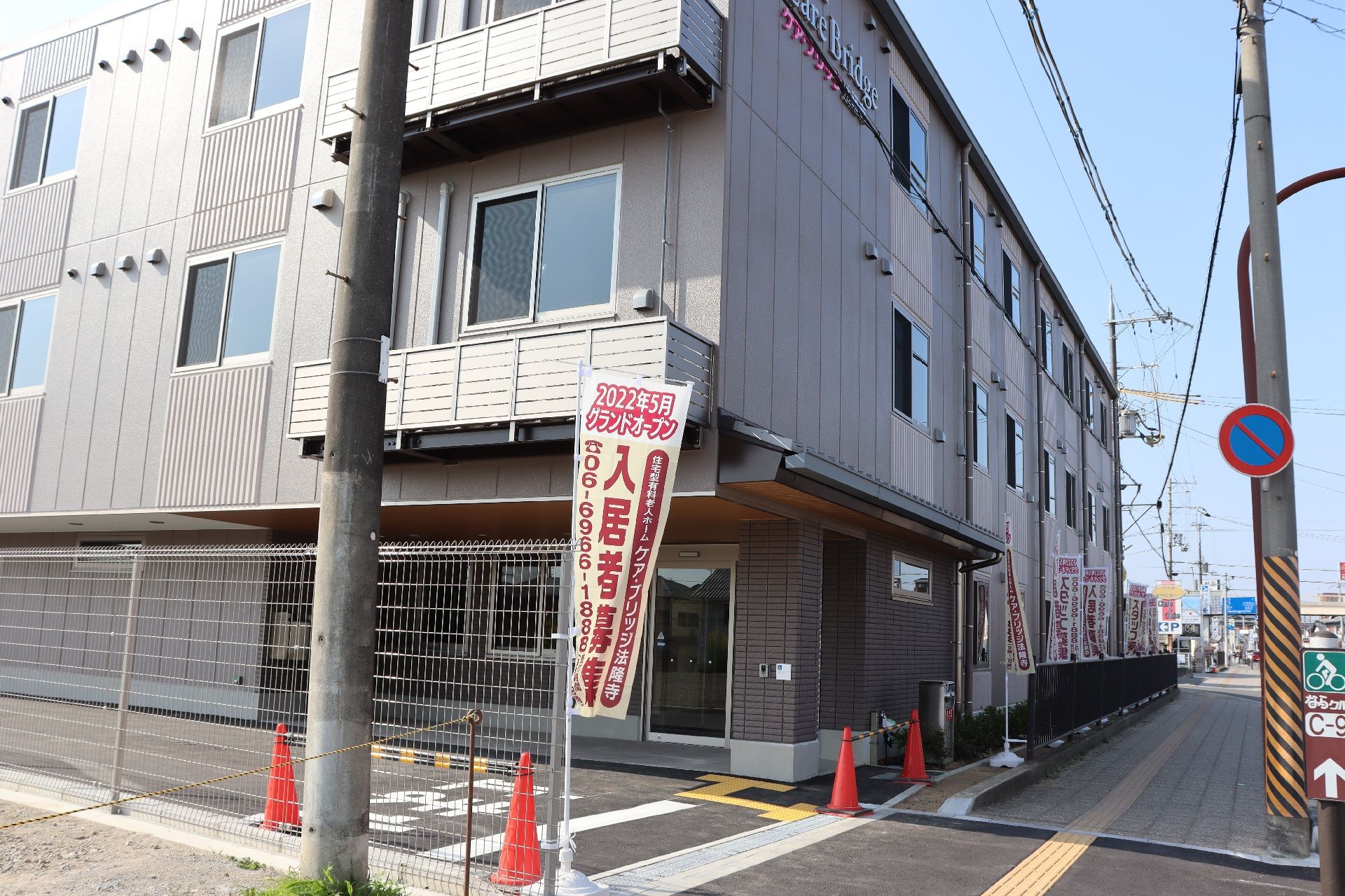 グレー系の外観の3階建ての建物で外壁にはホーム名が書かれ、玄関には瓦屋根が付いている。