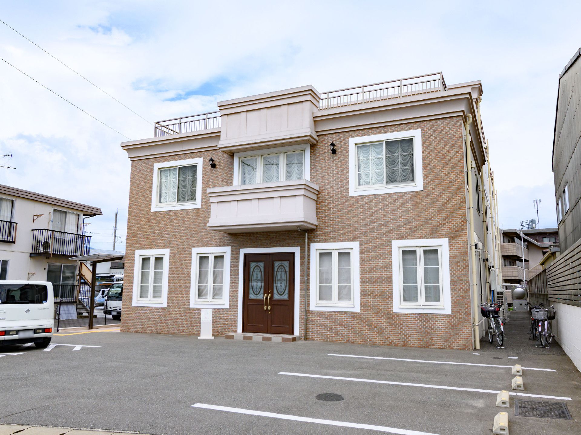 駐車場の奥に立地している２階建てのレンガ調の外観の建物