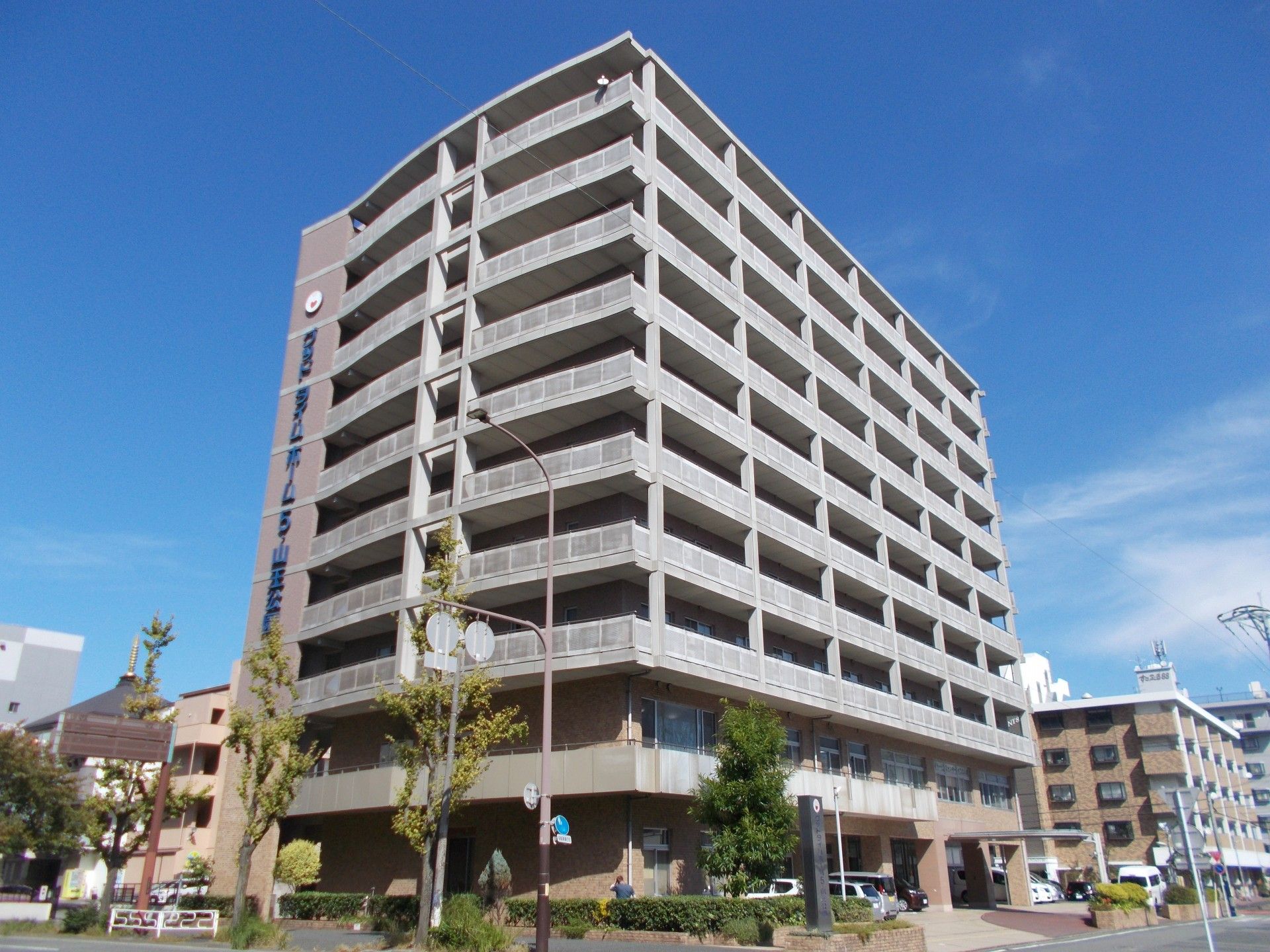 白を基調とした大きな建物。周辺には緑が多く、建物もたくさんあり、街中にある建物。