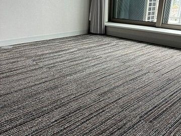 窓のそばまでカーペットが敷き詰められた居室のフロア。窓のカーテンは開けられていて明るい。