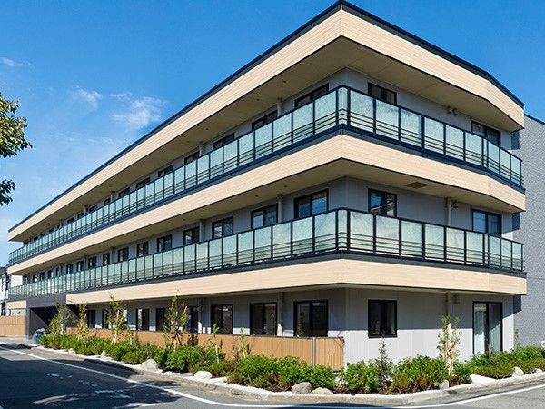 玄関前に木々が植えられている3階建ての建築物