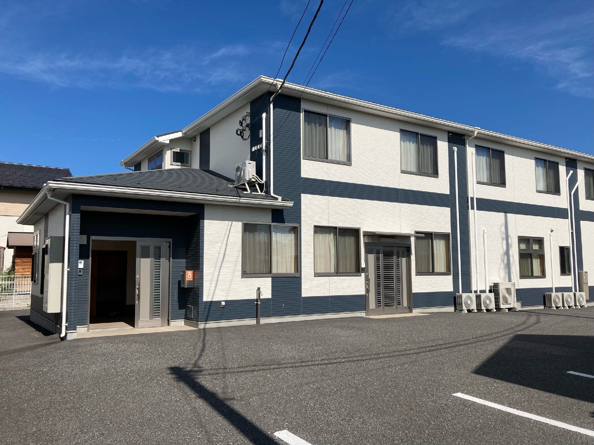 駐車場がある2階建ての建物は日当たり良好で、白とダークブルーの外壁。屋根も付いている。