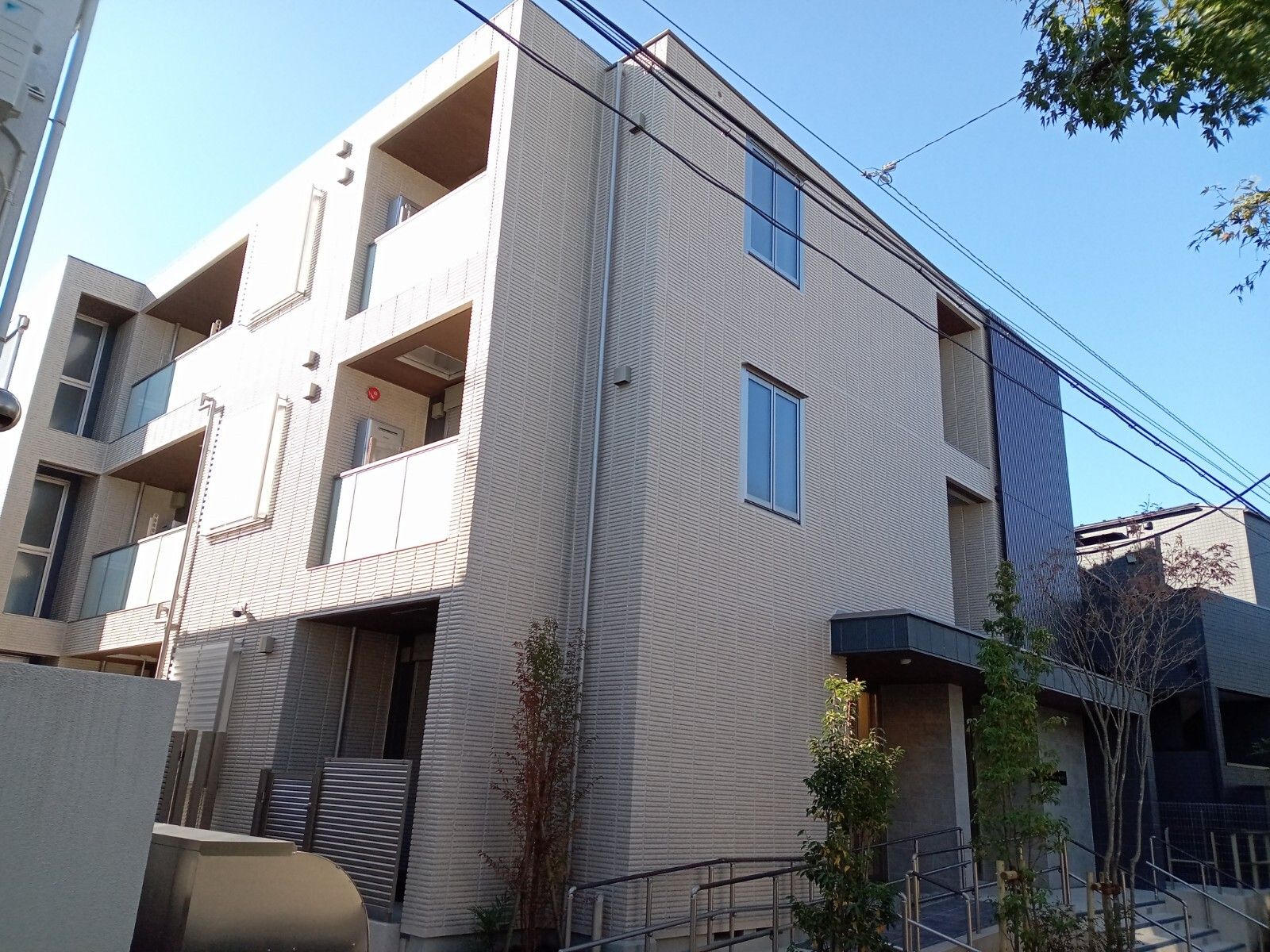 ベージュのとブラウンの外壁の3階建ての建物。建物の周りには草木が植えられ、玄関には緩やかなスロープと階段がある。
