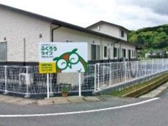 2階建ての建物はグレーの屋根が付き、周りには緑が多い。フクロウの絵が描かれた看板が立っている。