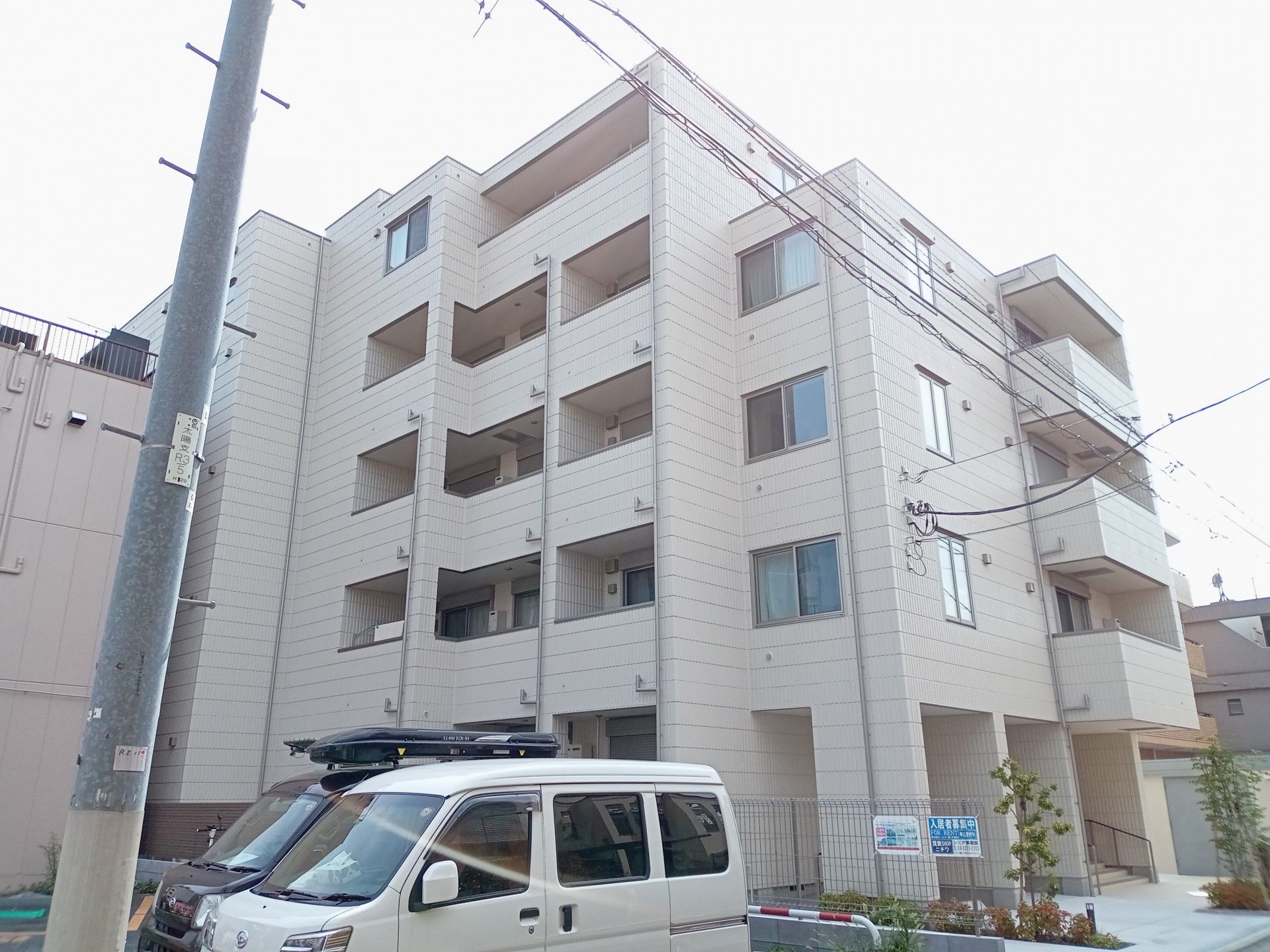 白を基調とした大きな建物の前には草木が植えられている。ブルーと白の館銘板もある。