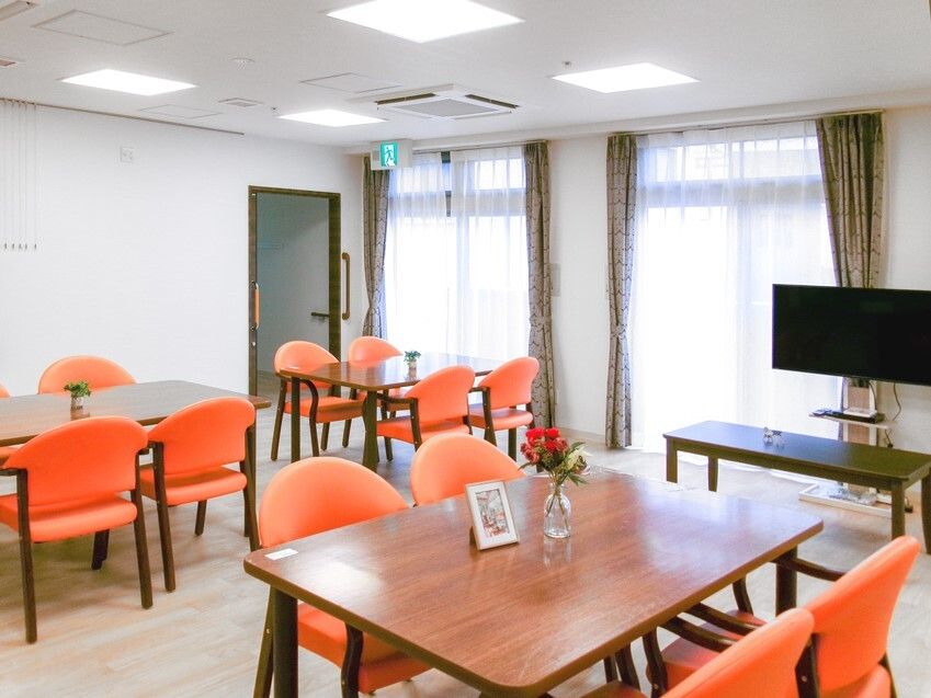 テレビが置かれているリビングダイニングにはオレンジの椅子がセットされたテーブルが置かれている。