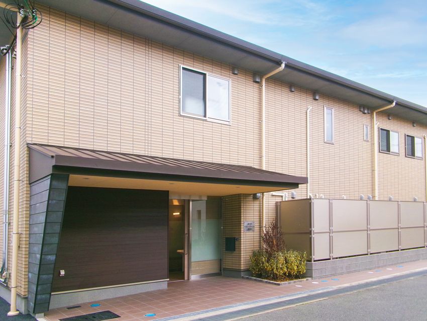 ブラウン系の建物は2階建てで横に長く、玄関には大きな車寄せが付いている。