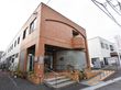 茶色のタイル状の壁の奥に長い建物になっている。入り口まで階段と折り返しのあるスロープがついており手すりも設置されている。