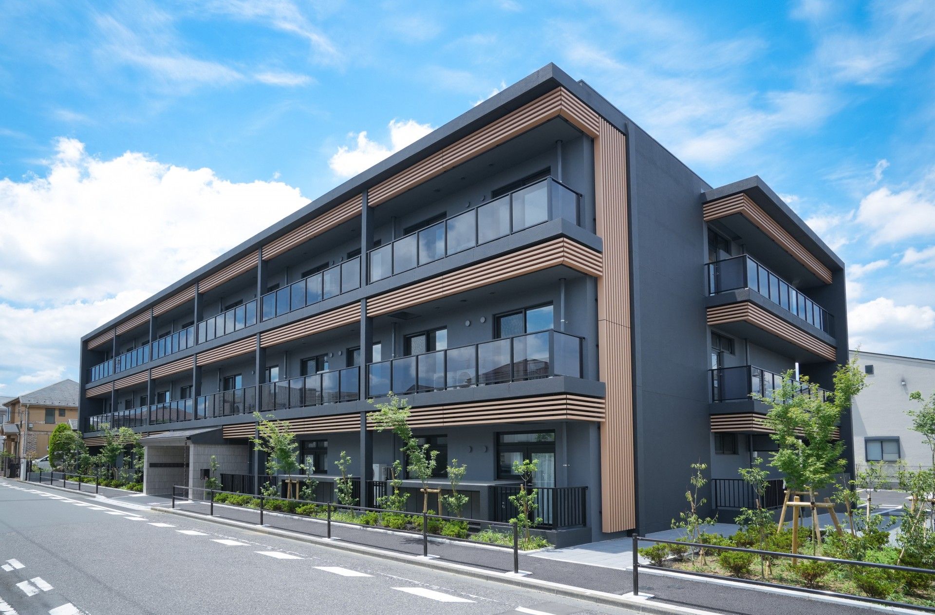 周囲が緑に囲まれており、濃いグレーの外壁のバルコニー付き3階建て建築物