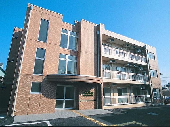 3階建ての大きな建物。入り口には手すりや点字ブロックが設置され、大きなひさしもあり雨の日にぬれる心配がない。