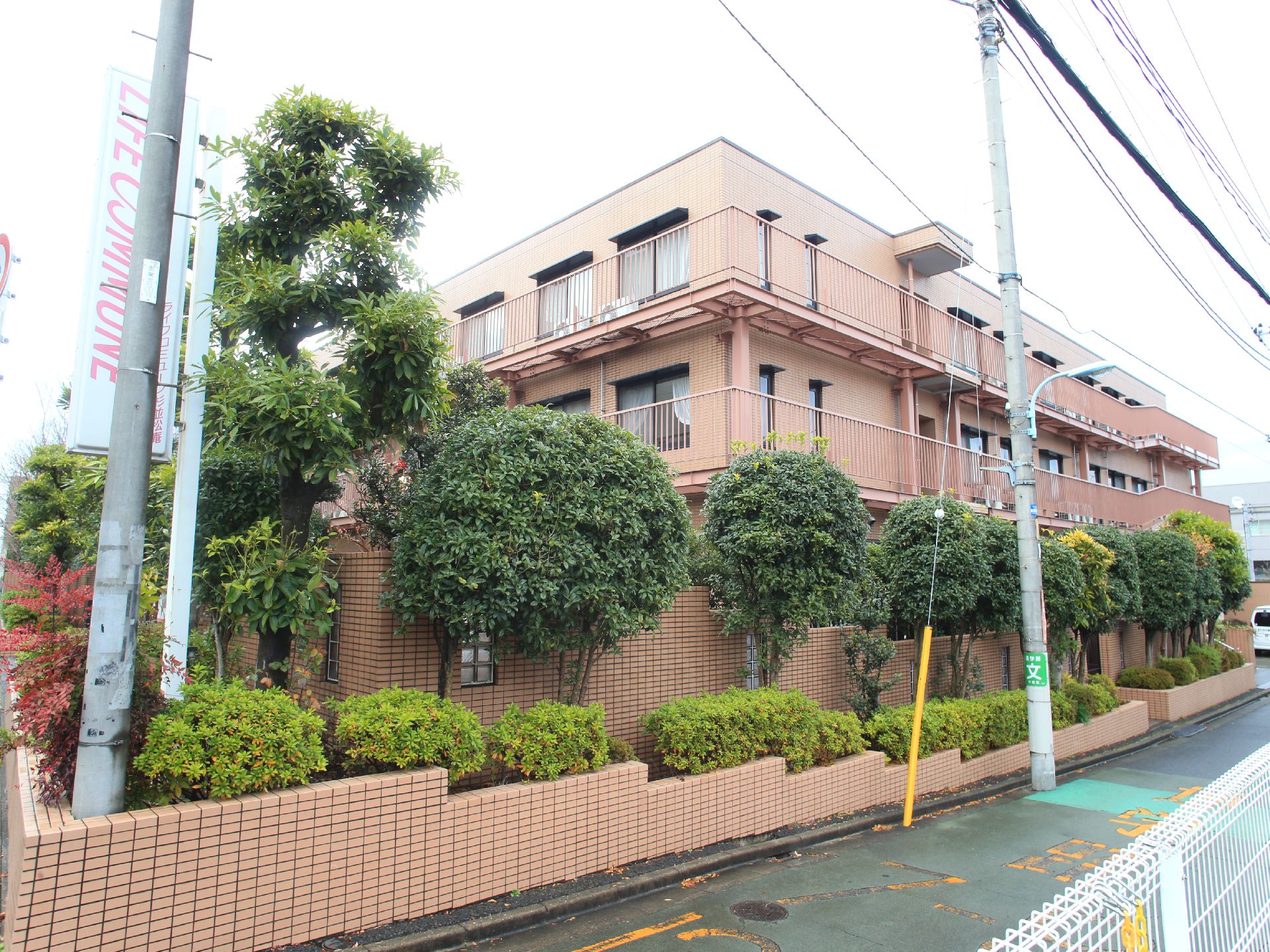 赤茶色の建物になっており隣を道路がのびている。ブロック状の茶色の塀でまわりを囲まれており樹木も多く茂っている。