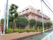 赤茶色の建物になっており隣を道路がのびている。ブロック状の茶色の塀でまわりを囲まれており樹木も多く茂っている。