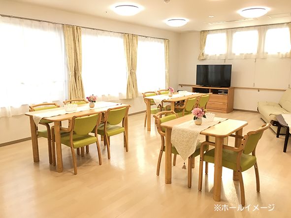 テーブル、椅子の置かれた広いダイニングである。壁には写真や貼り絵が飾られている。椅子やドアのピンク色が優しい雰囲気である。