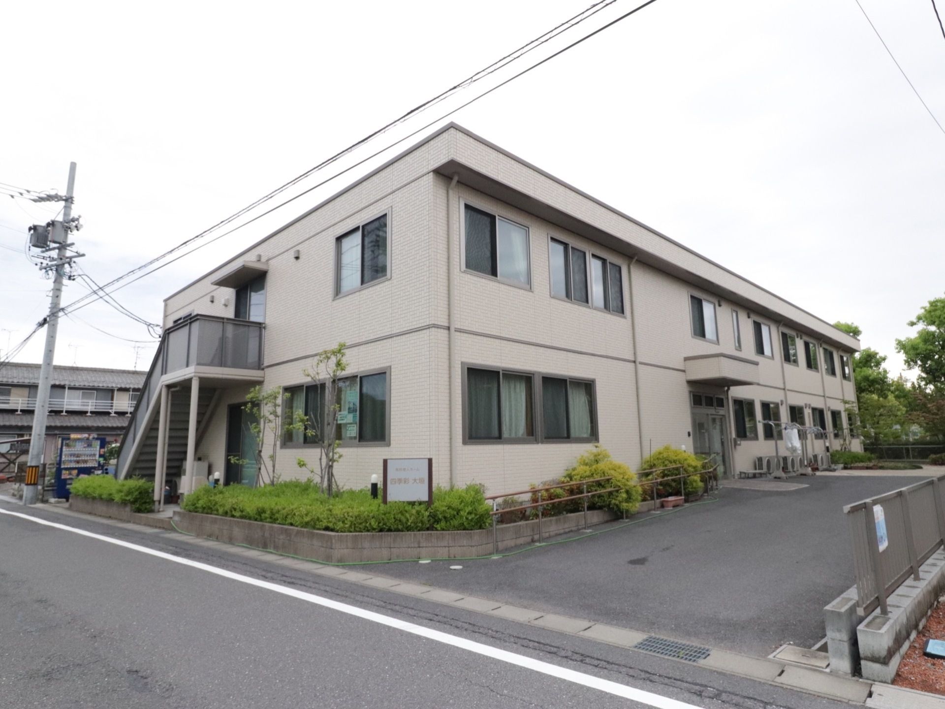 施設の建物は２階建てで、クリーム色を基調とした外観である。建物の周りには大小さまざまな植栽が植えられている。